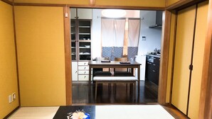 Um quarto japonês tradicional com tatames, uma mesa baixa com uma tigela e um menu, e portas deslizantes que dão para uma cozinha.