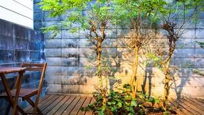A wooden deck with a table and chairs, a small tree, and a stone wall. - Kyomusha Inn (Kyoto)