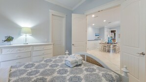 A bedroom with a bed, dresser, lamp, and a view into the dining area. - Sleeps 10  Beach-Bay Views Private Heated Pool Elevator Perfect location (Holmes Beach)