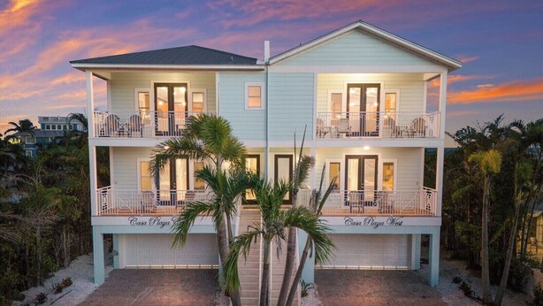 A two-story beachfront property with balconies, palm trees, and a well-maintained garden. - Sleeps 10  Beach-Bay Views Private Heated Pool Elevator Perfect location (Holmes Beach)