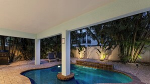 An outdoor swimming pool with a curved design, surrounded by a brick patio and palm trees. - Sleeps 10  Beach-Bay Views Private Heated Pool Elevator Perfect location (Holmes Beach)