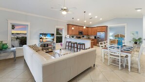A spacious living room with a white sofa, a TV, and a dining area with a wooden table and chairs. - Sleeps 10  Beach-Bay Views Private Heated Pool Elevator Perfect location (Holmes Beach)
