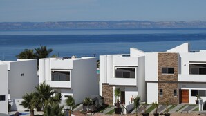 A modern building with a flat roof, white walls, and a stone accent wall. It has a large window and a door with a number sign. - House 255 Torres Cantera (La Paz)