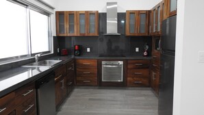A kitchen with wooden cabinets, a stainless steel dishwasher, and a black refrigerator. - House 255 Torres Cantera (La Paz)