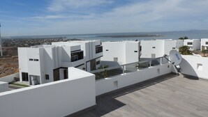 A modern residential building with a flat roof, satellite dish, and a view of the sea and distant cityscape. - House 255 Torres Cantera (La Paz)