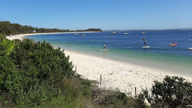 A beach with clear blue water, kayaks, and boats.