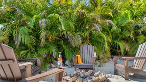 Un coin salon aménagé sur la plage, avec deux chaises en bois, une petite table et une bouteille de bière.