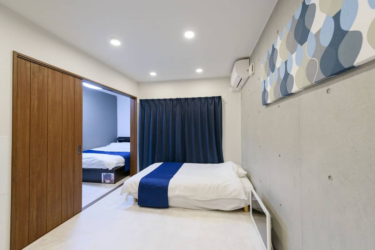 A hotel room with a bed, a wardrobe, a mirror, a window with curtains, and a wall-mounted air conditioning unit.