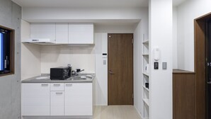 A compact kitchen with white cabinets, a microwave, a sink, and a wooden door. - HOTEL Ciel Hills (Tokyo)