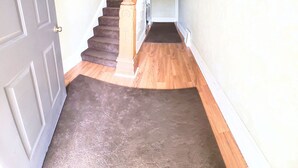 Un corridoio con pavimento rivestito di moquette, una scala in legno e una porta.