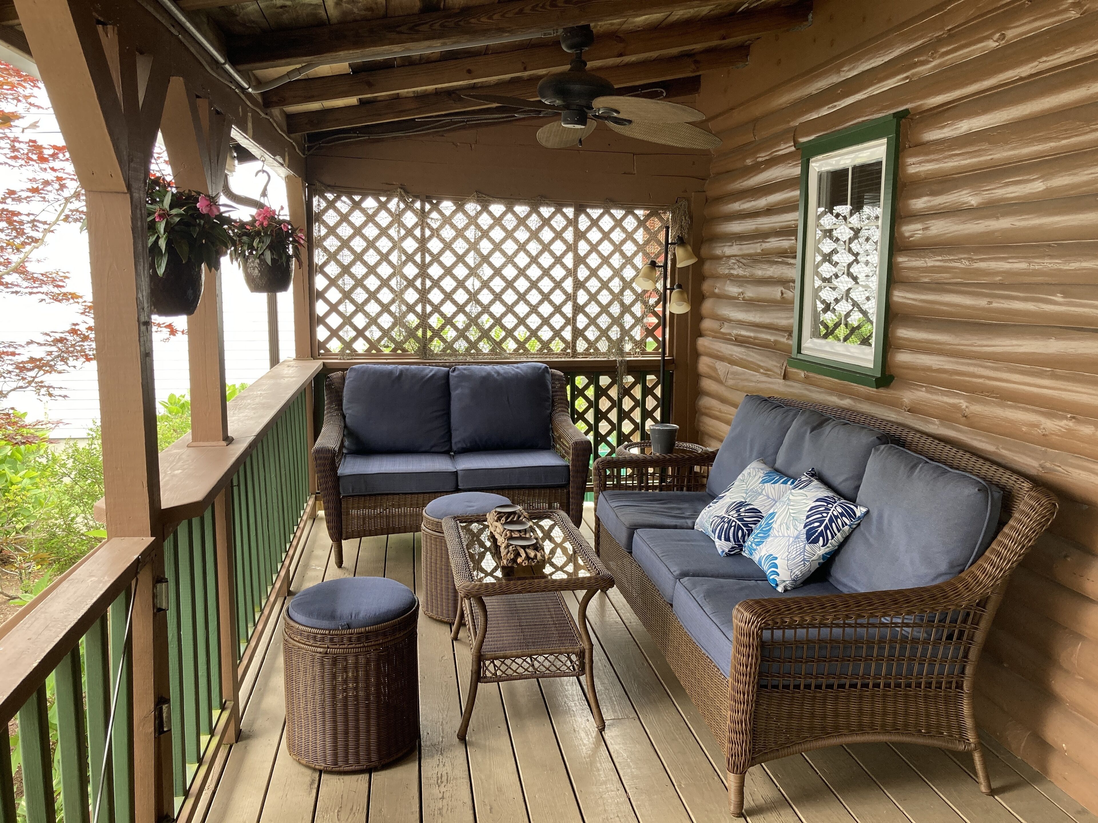 A wooden deck with wicker furniture, including sofas and a table, and a ceiling fan.
