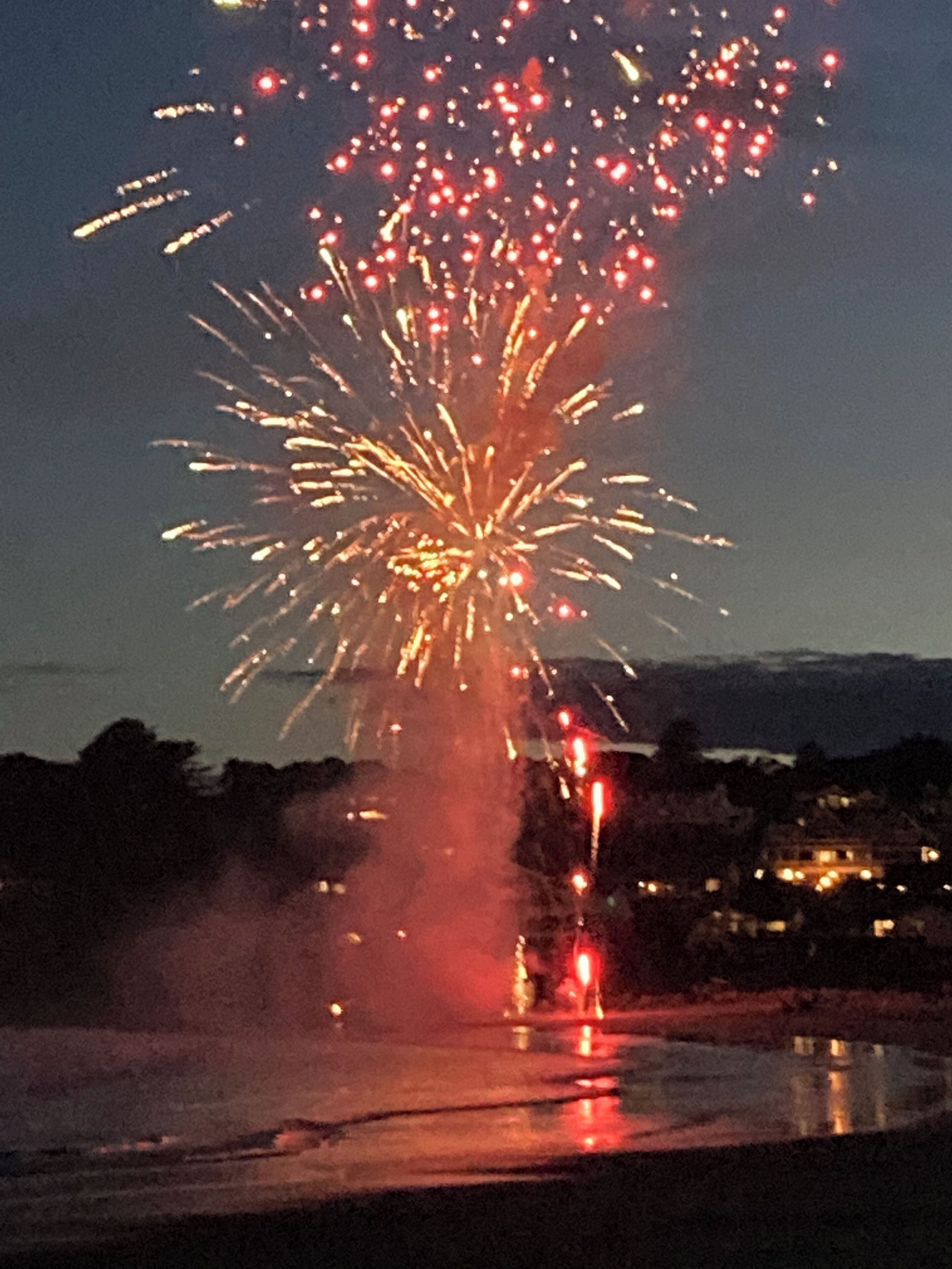 A nighttime scene with fireworks over a body of water, reflecting lights from nearby buildings.