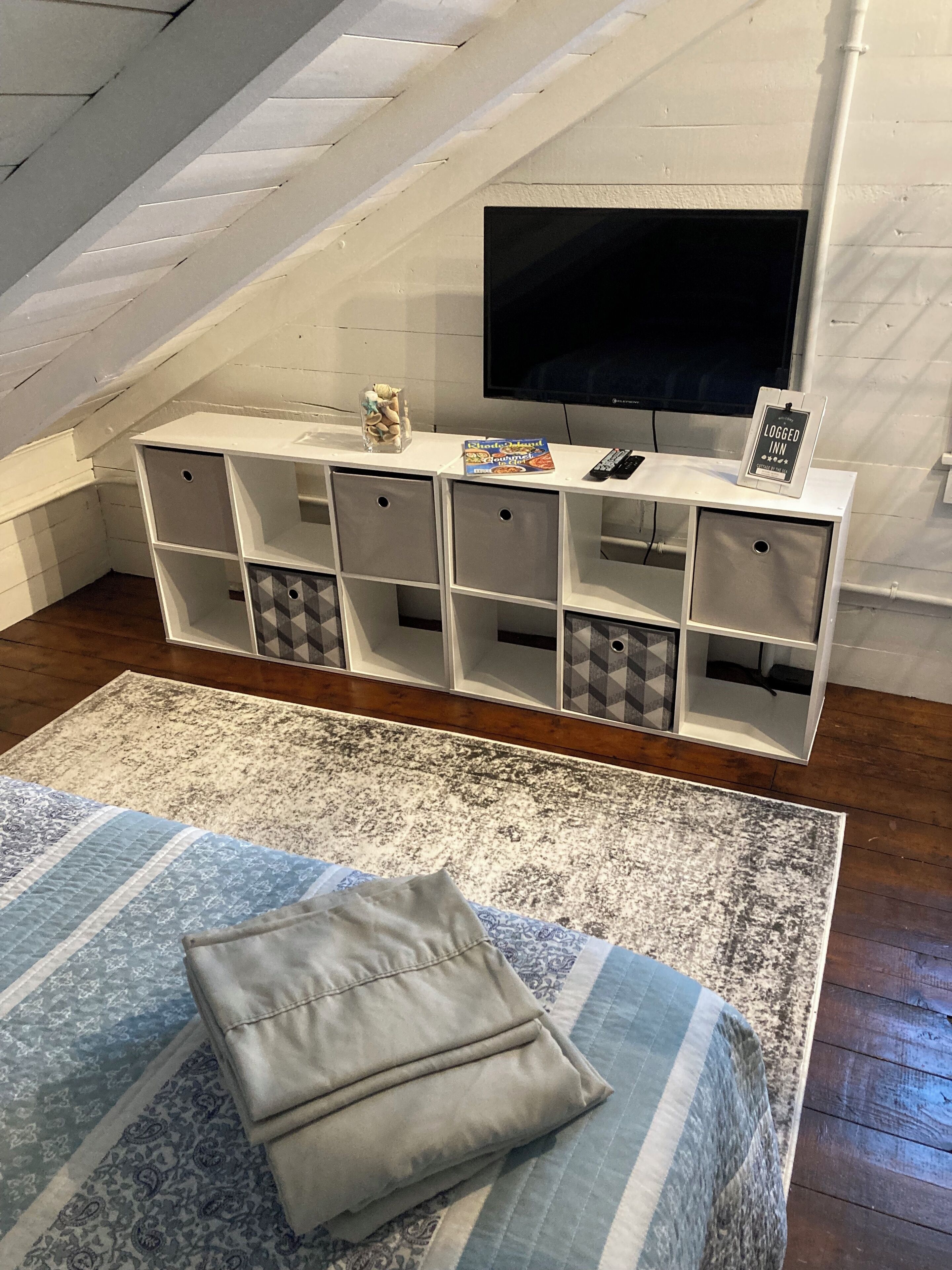 A cozy attic bedroom with a large TV, storage units, and a bed with a patterned bedspread.