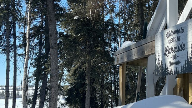 Une terrasse en bois avec un banc recouvert de neige et une pancarte accueillant les visiteurs au Great Slave Lakeside B&B.