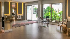A modern hotel lobby with a glass door leading to a balcony, clear chairs, a small table, and a patterned rug. - Apartamento de 2 Quartos no Luxuoso Condomínio Jay (Jurerê Internacional)