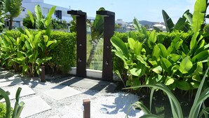 A garden pathway with a modern gate, surrounded by lush greenery and a clear sky. - Apartamento de 2 Quartos no Luxuoso Condomínio Jay (Jurerê Internacional)