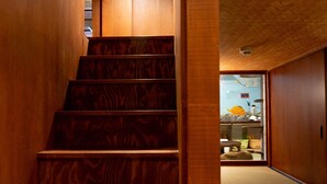 Una escalera de madera con diseño tradicional que conduce a una habitación con suelo de tatami y vistas a un comedor.