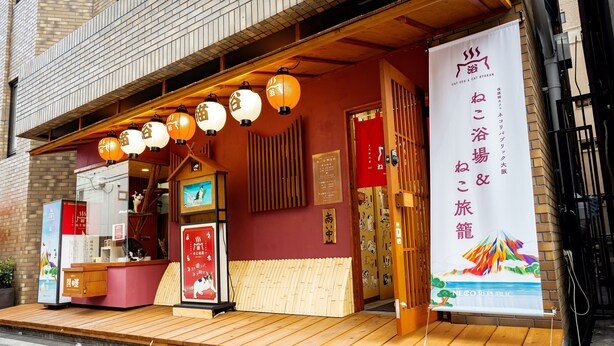 Un edificio japonés tradicional con fachada de madera, entrada roja y un letrero anunciando un spa felino y un ryokan para gatos.