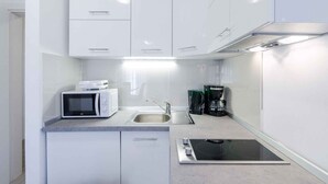 A modern kitchen with white cabinets, a microwave, a coffee maker, and an induction cooktop. - Holiday apartment with balcony and air conditioning (Crikvenica)