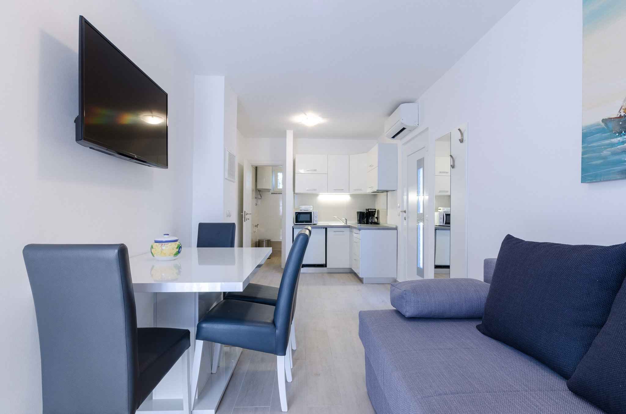 Eine moderne Küche mit weißen Schränken, ein Essbereich mit Tisch und Stühlen sowie ein graues Sofa.