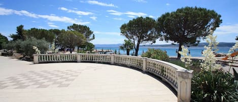A curved outdoor terrace with a checkered floor, surrounded by a balustrade, overlooking a body of water and trees.