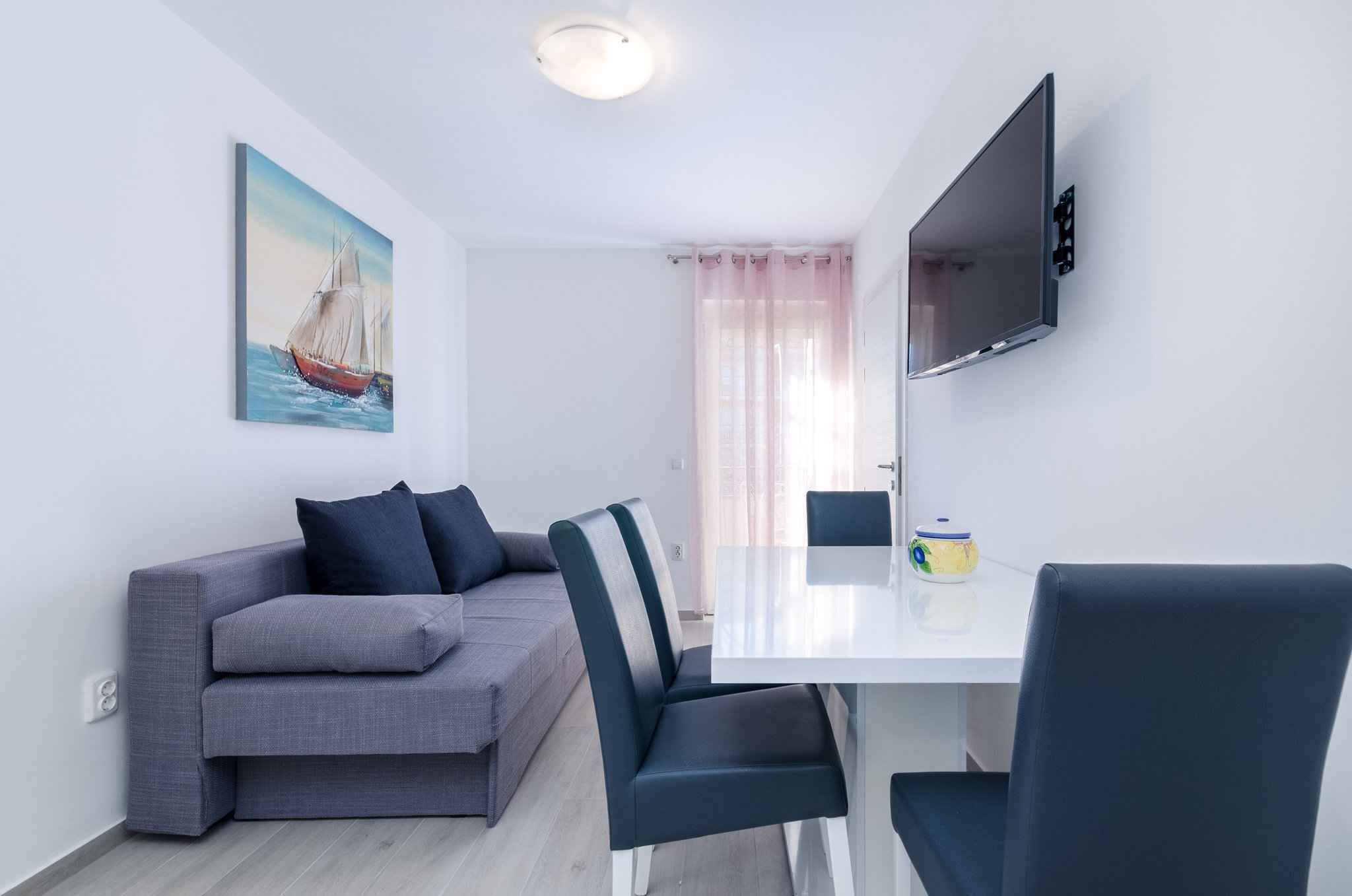 Una sala de estar moderna con un sofá gris, una mesa de comedor y un televisor de pantalla plana montado en la pared.