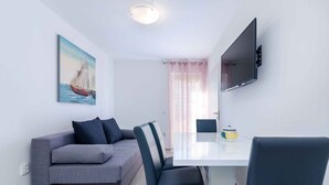 A modern living room with a grey sofa, a dining table, and a flat-screen TV mounted on the wall. - Holiday apartment with balcony and air conditioning (Crikvenica)