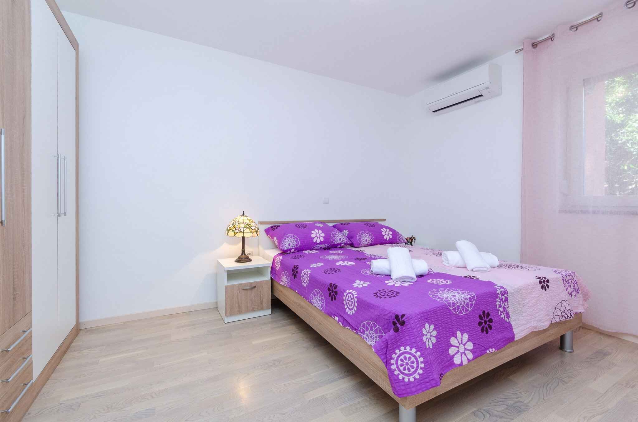 Een slaapkamer met een bed, nachtkastje, lamp en een raam met gordijnen.