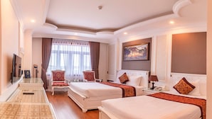 A hotel room with two beds, a sitting area with chairs, a large window with curtains, a painting on the wall, and a wooden floor. - HANZ Premium Mai Vang 2 Hotel Dalat (Xuan Huong - Da Lat)