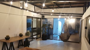 Habitació espaiosa amb taula de fusta, tamborets negres, cadiretes penjants i plantes en testos.
