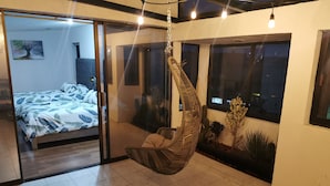 Una habitació moderna amb una cadira penjant, un llit amb un llençol estampat i vista a l'exterior a través de grans finestres.