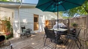 Une terrasse avec une table et des chaises, un parasol vert et un barbecue.