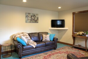 A living room with a brown leather sofa, a television on a stand, a painting on the wall, and a patterned rug. - Conveniently Located close to downtown.  No stairs to climb. (Livingston)