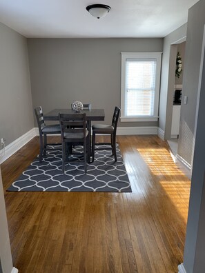 A dining area with a table and chairs, a patterned rug, and a window with blinds.