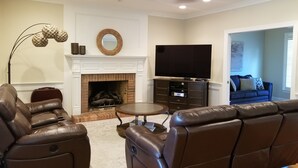 Un salon avec une cheminée, des canapés en cuir, un téléviseur et un ventilateur de plafond.