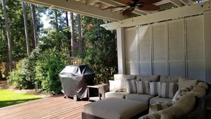 Une terrasse couverte avec un canapé en osier, un barbecue et un ventilateur de plafond.