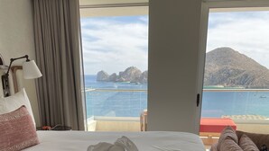 Habitación de hotel con cama, vista al mar y balcón con una silla roja.
