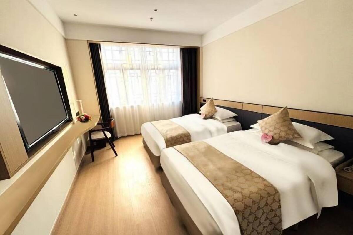 A hotel room with two beds, a TV, a chair, and a window with curtains.