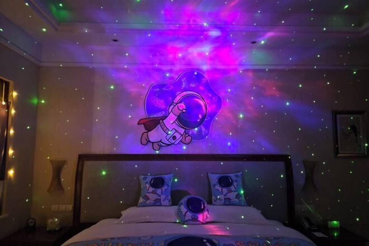 A bedroom with a bed, two pillows, a nightstand, and a wall with a space-themed design.