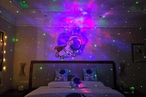 A bedroom with a bed, two pillows, a nightstand, and a wall with a space-themed design. - Tianjin Binhai One Hotel (HUANGGANG COMMUNITY BINHAI NEW)