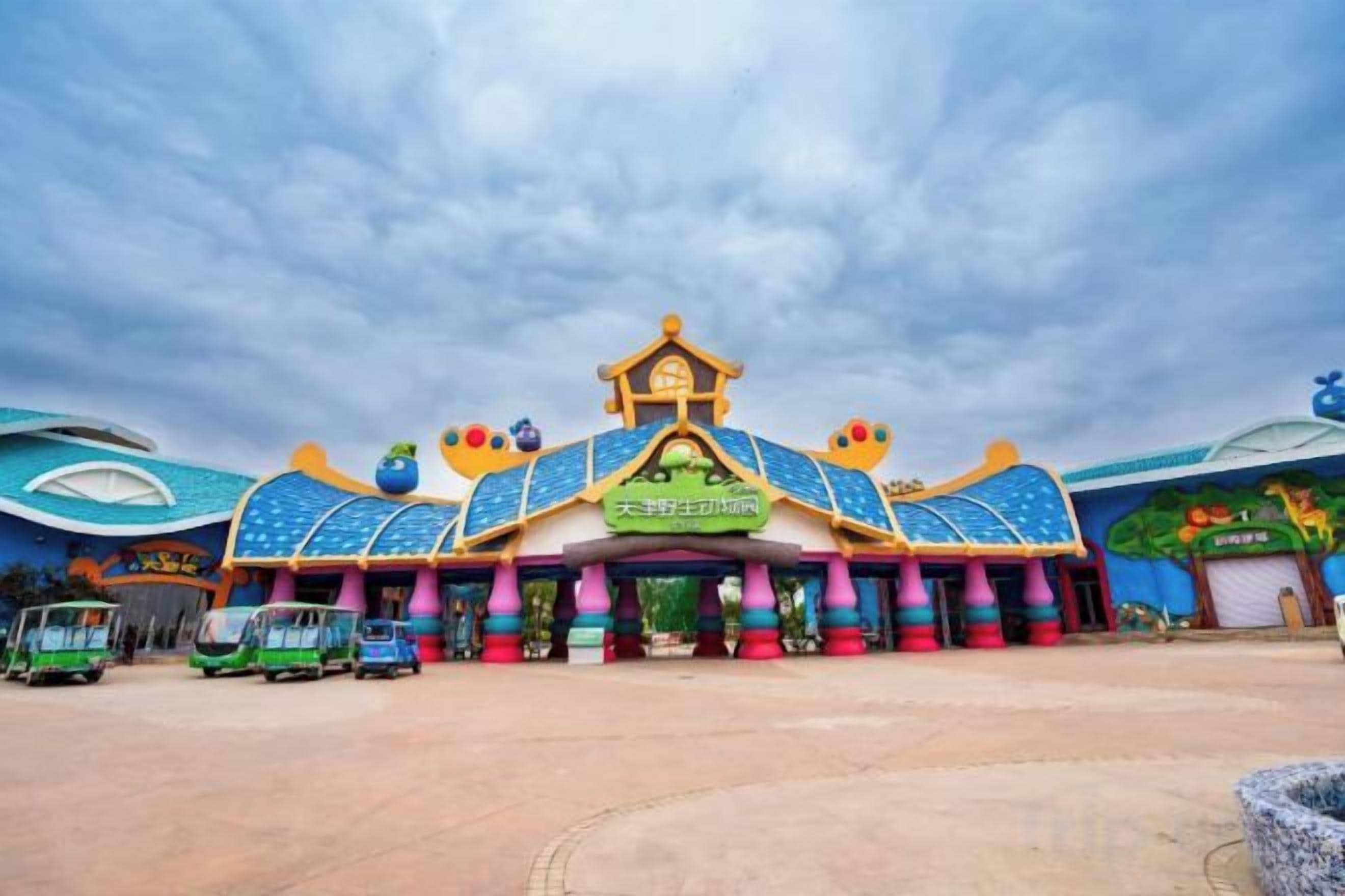 A colorful building with a central entrance, surrounded by a parking area with vehicles.