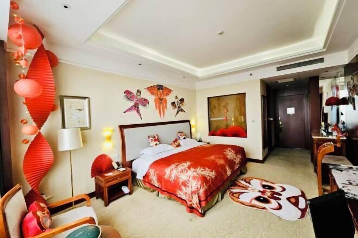 A hotel room with a bed, bedside table, lamp, and a wall with artwork.