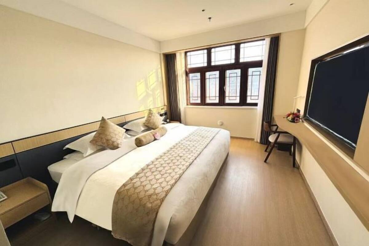 A hotel room with a bed, bedside table, window, and a flat-screen TV.