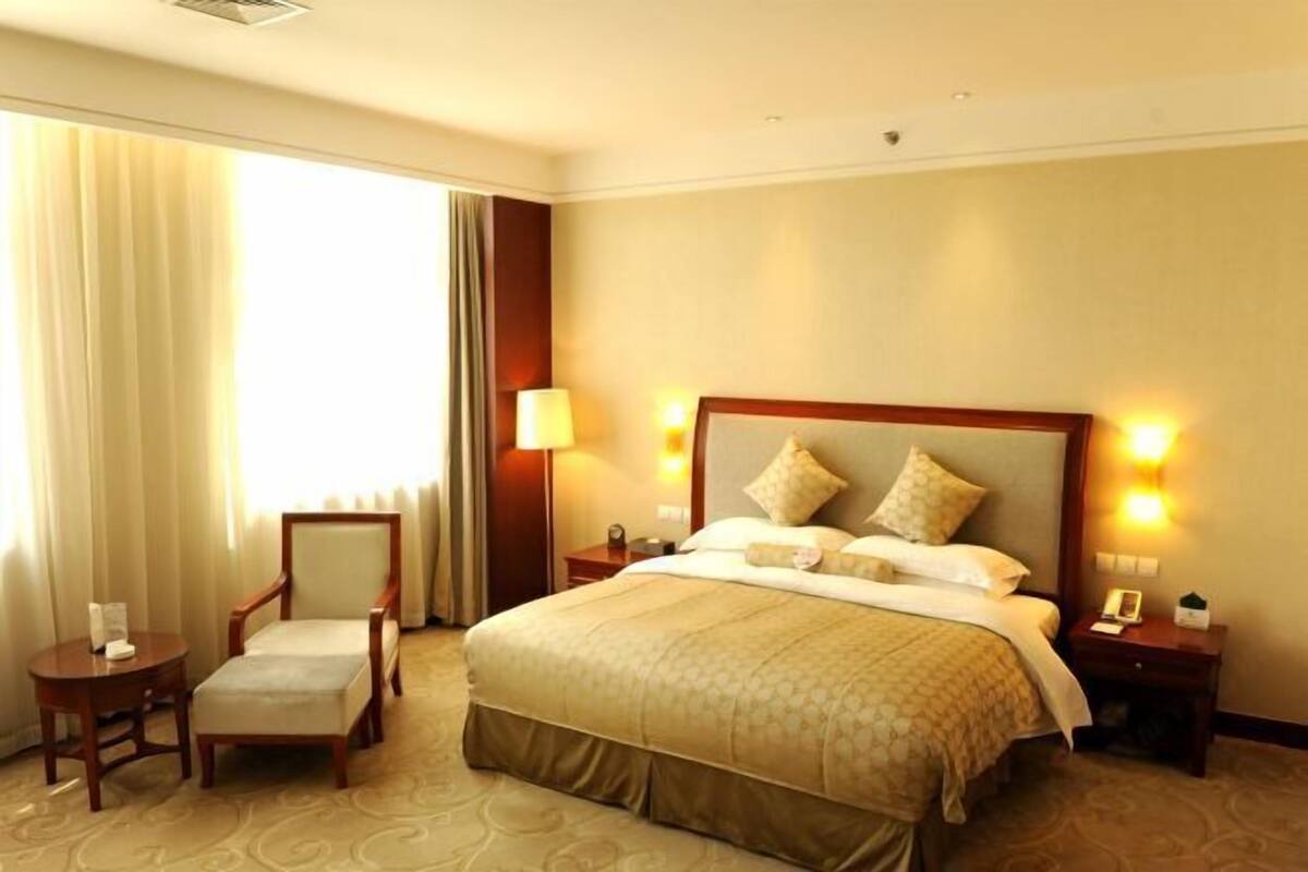 A hotel room with a large bed, two bedside tables, a chair, a lamp, and a window with curtains.