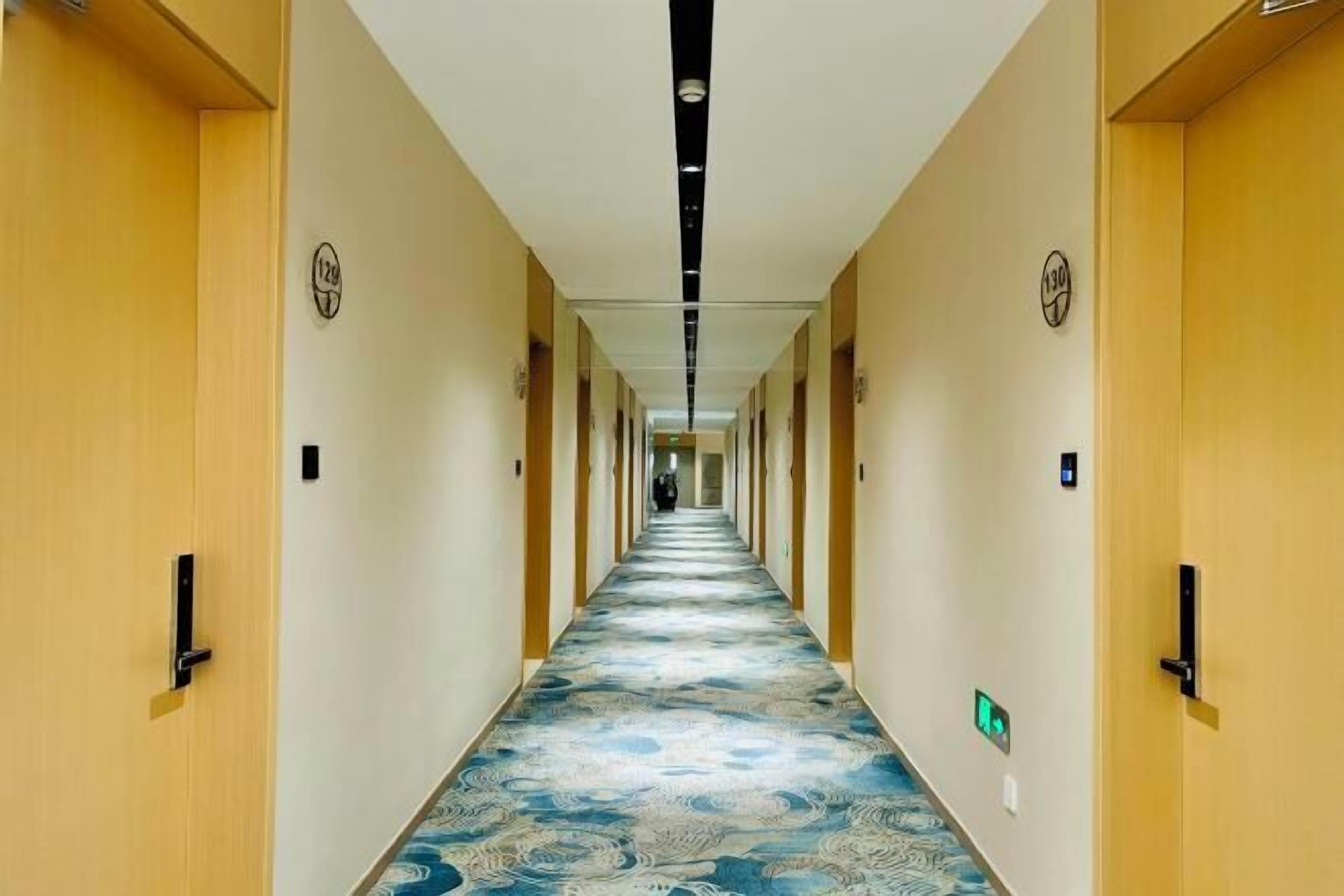 A hotel hallway with a patterned carpet, wooden doors, and a long corridor.