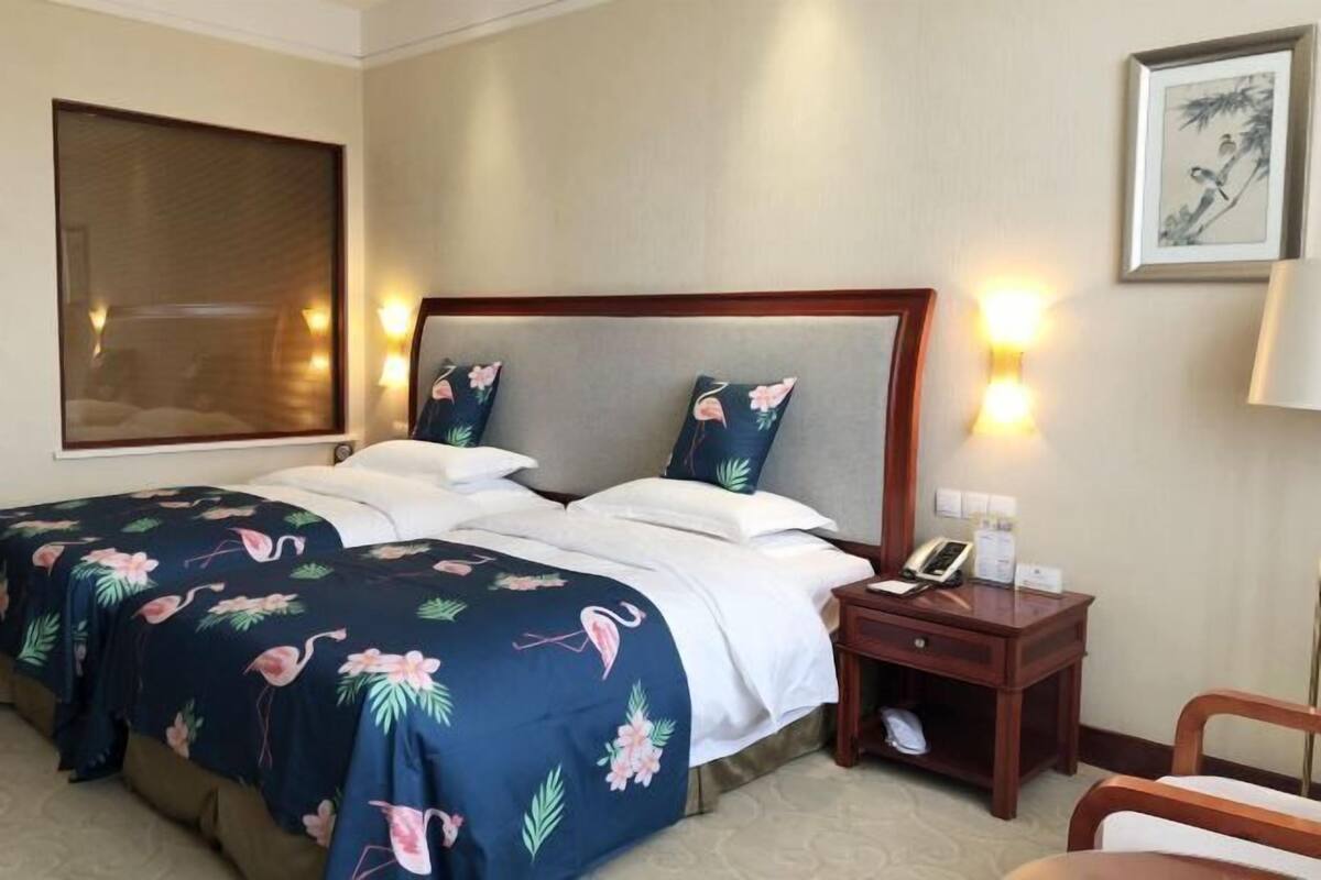 A hotel room with a bed, bedside table, lamp, and a framed picture on the wall.
