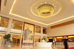 A spacious lobby with a high ceiling, a large chandelier, and a reception desk.