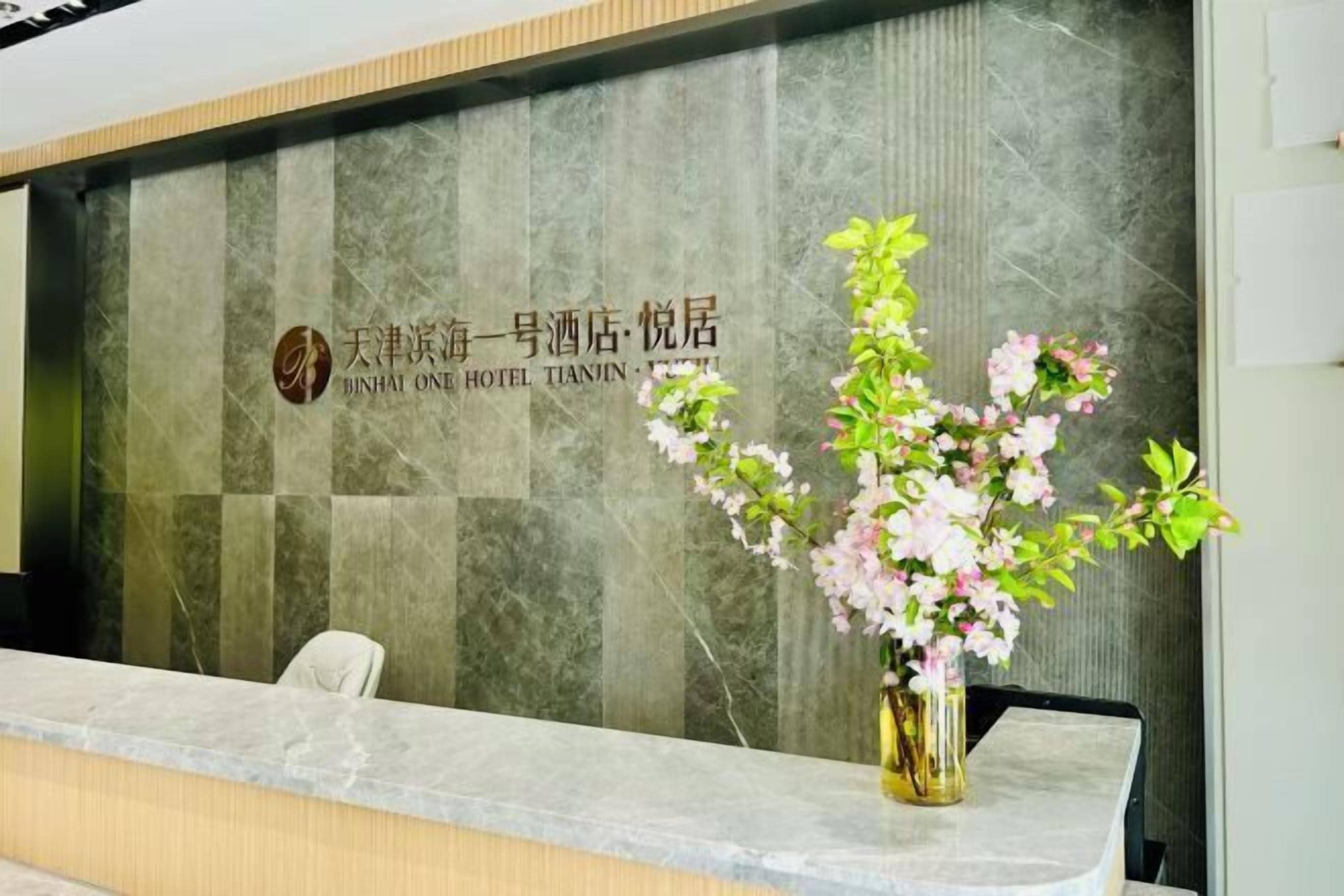 A reception desk with a marble counter and a vase of pink flowers.