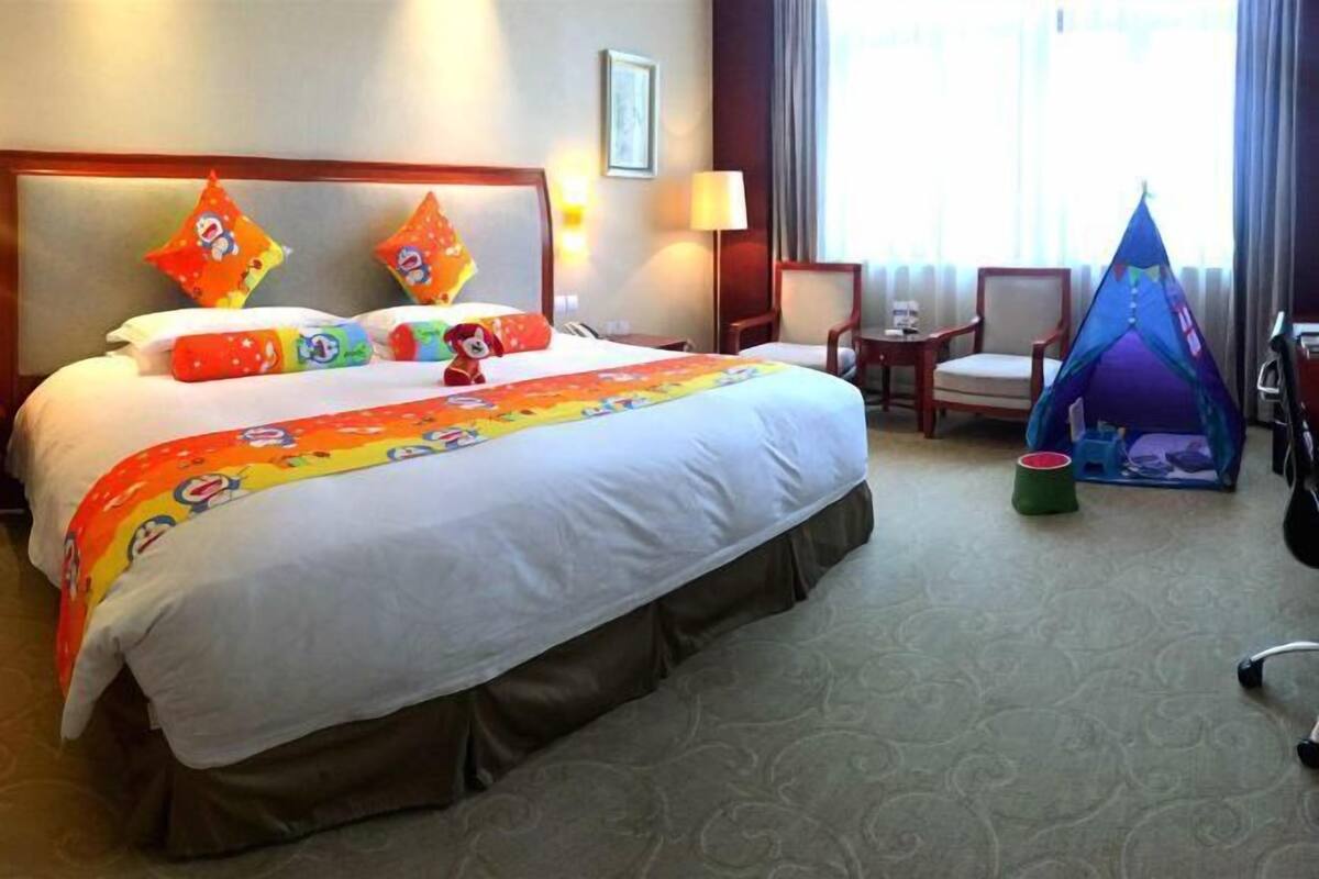A hotel room with a large bed, a headboard, a nightstand, a lamp, a chair, a small table, and a window with curtains.