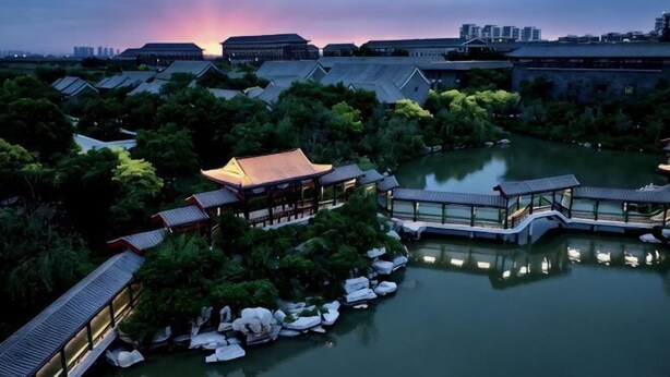 Een traditioneel Japans gebouwcomplex met meerdere gebouwen, een waterpartij en een ondergaande zon op de achtergrond.